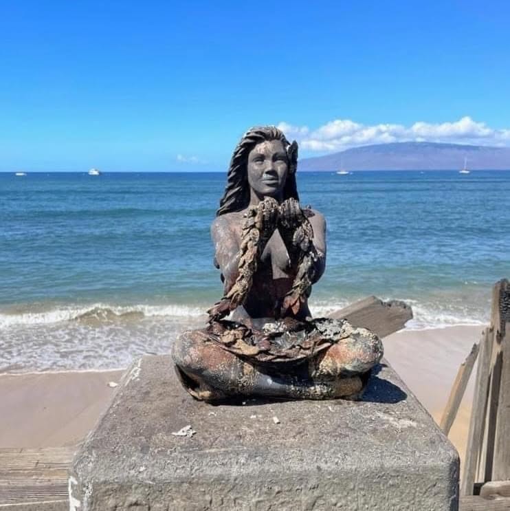 The scorched bronze statue of the same figure, still holding her lei, on the shore at Lahaina
